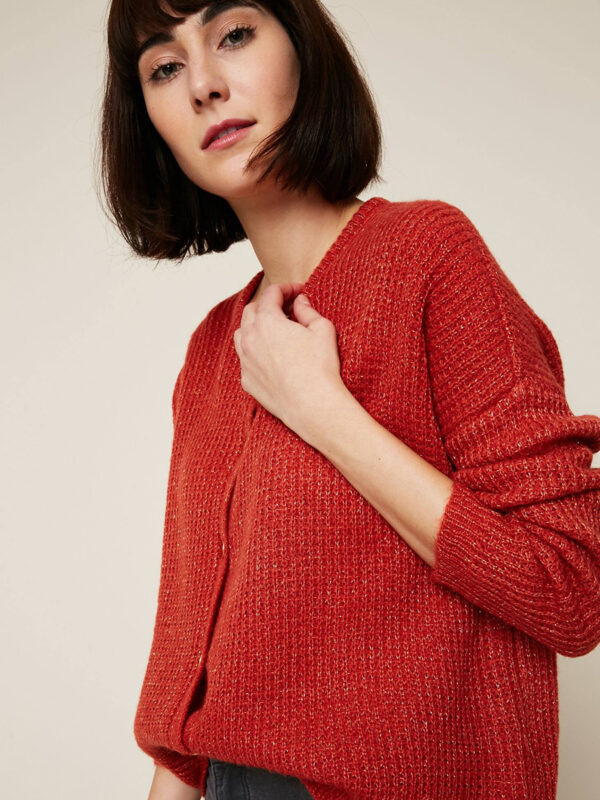 A woman in red sweater standing next to wall.
