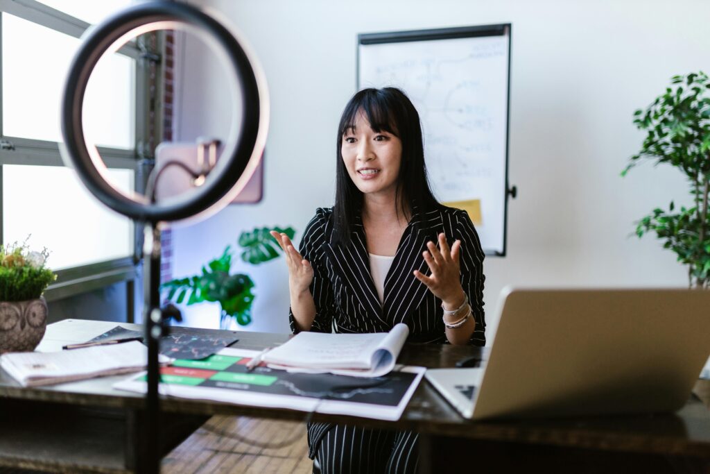 Woman recording a video by her desk with a phone and ring light.